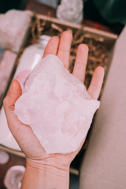 Close-up of a hand holding a raw rose quartz crystal, highlighting its texture and pink hue.